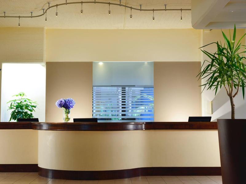 Moderne hotelreceptie met planten, een gebogen balie en slingerverlichting aan het plafond.