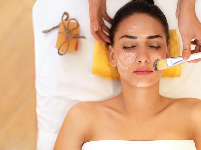 Een vrouw krijgt een gezichtsbehandeling liggend met gesloten ogen en een borstel op haar gezicht.
