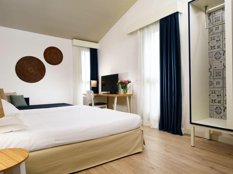 Lichte hotelkamer met groot bed, houten vloer, bureau en decoratieve wandkunst.