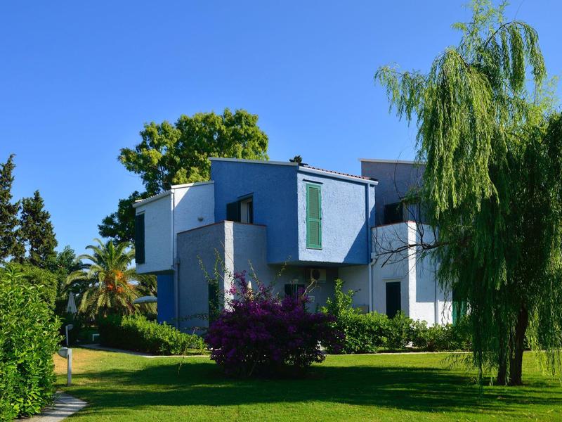 Modern wit huis met blauwe accenten omgeven door groene bomen en een heldere blauwe lucht.