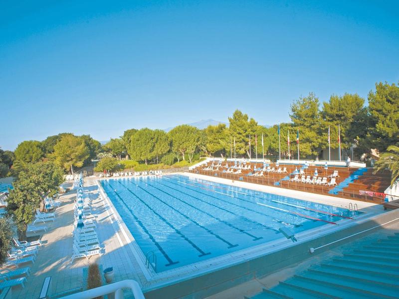 Groot hotel omgeven door tuinen en een zwembad met bergen op de achtergrond.