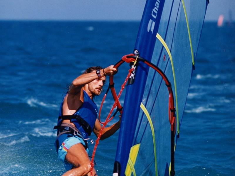 Persoon aan het windsurfen op blauwe oceaan onder heldere lucht, houdt zeil stevig vast op wit board.