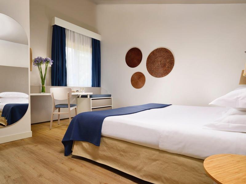 Knusse hotelkamer met een bed, houten vloer, bureau en wanddecoratie met cirkelvormen.