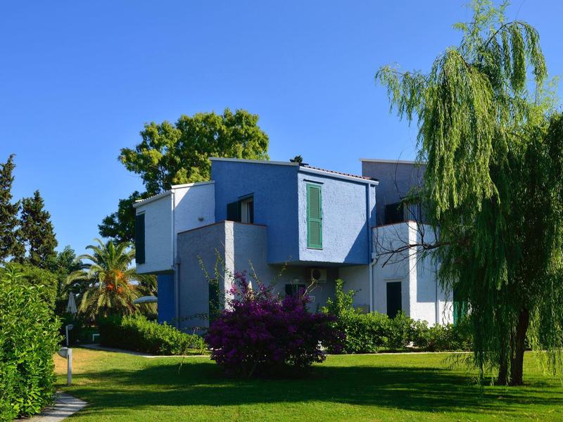 Modern wit hotelgebouw omgeven door weelderige groene bomen en een helderblauwe lucht.