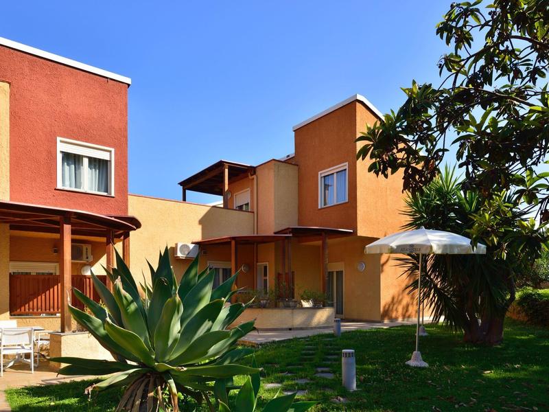 Kleurrijke vakantiehuizen met tuin, terrasmeubilair en een heldere blauwe lucht op de achtergrond.