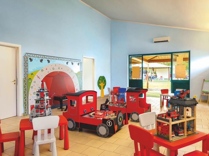 Lichte kinderkamer met rood-witte meubels, speelgoed en groot raam voor daglicht.