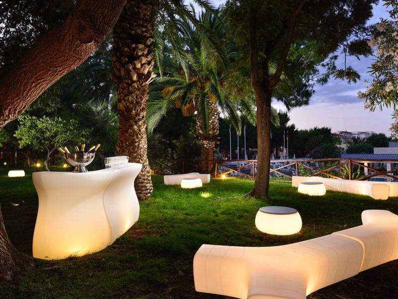 Buitenlounge met gloeiend meubilair omringd door palmbomen bij schemerlicht.