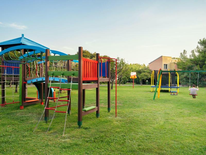Een kleurrijke speeltuin met schommels en klimrekken op groen gras onder een heldere lucht.
