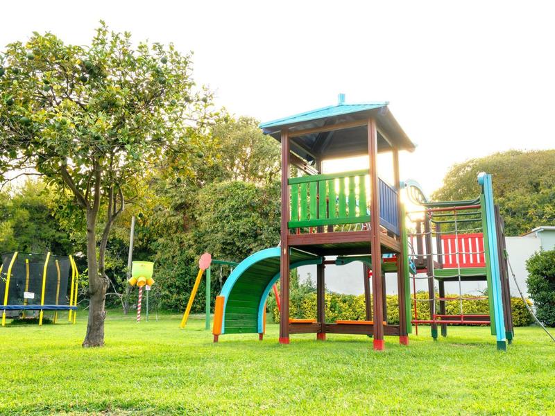 Speeltuin met glijbanen en klimtoestellen omringd door gras en bomen onder een heldere lucht.