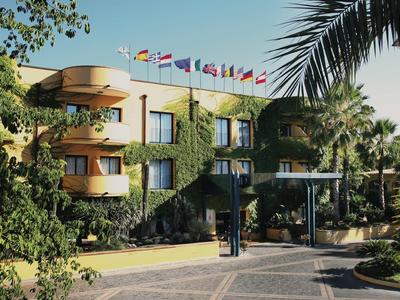 Mehrstöckiges Hotelgebäude mit Fahnen, begrüntem Fassade und Palmen im Eingangsbereich.