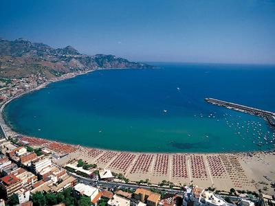 Vista aérea de una ciudad costera con playa y mar azul bajo cielo despejado.