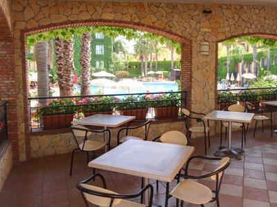 Terraza cubierta con mesas y sillas, vista a una piscina y área de jardín.