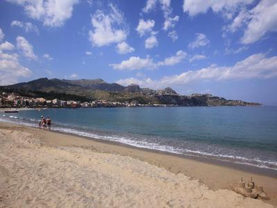 Playa con arena, mar tranquilo y montañas al fondo bajo cielo azul con nubes.