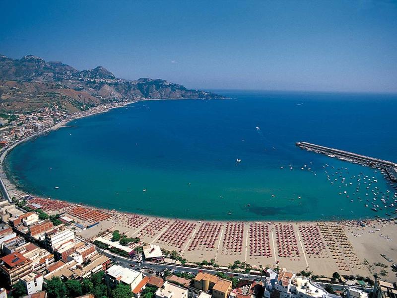 Vista aérea de una ciudad costera con playa y mar azul bajo cielo despejado.