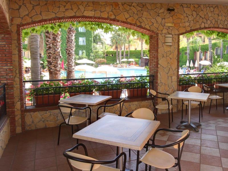 Terraza cubierta con mesas y sillas, vista a una piscina y área de jardín.