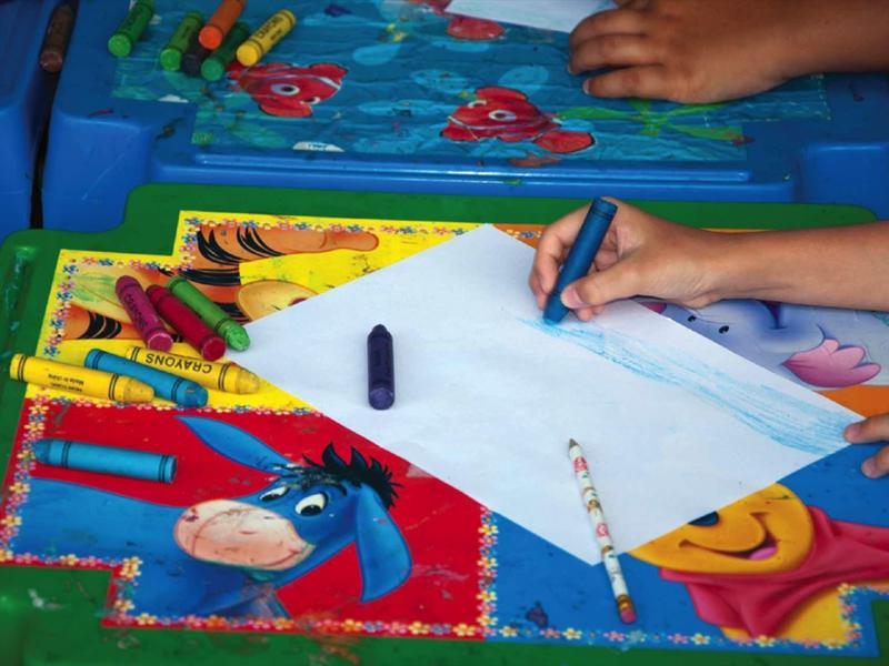 Niños dibujan con lápices de colores sobre una mesa con tela colorida.