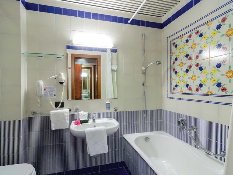 Baño luminoso con bañera, lavabo y azulejos coloridos en la habitación del hotel.