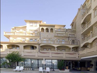 Großes helles Hotel mit mehreren Balkonen und einem blauen Pool im Vordergrund bei klarem Himmel.