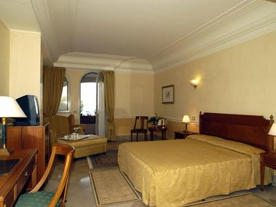 Gemütliches Hotelzimmer mit Doppelbett, Schreibtisch, Fernseher und Stuhl in warmen Beigetönen.