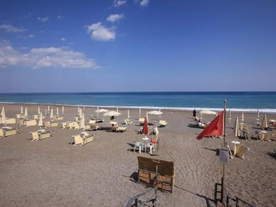Ein ruhiger Sandstrand mit vielen Liegestühlen und Sonnenschirmen unter einem blauen Himmel.