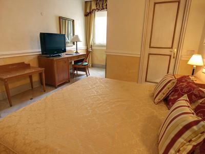 Gemütliches Schlafzimmer mit Doppelbett, Fernseher, Schreibtisch, Stuhl und Fenster mit Vorhang.