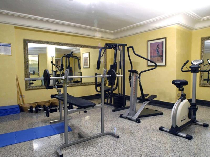 Kleines Fitnesszimmer mit gelben Wänden, Spiegeln und Geräten wie Fahrrad, Stepper und Hantelbank.