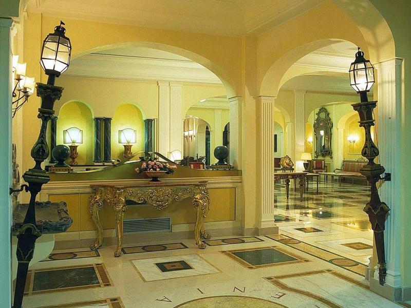 Heller Eingangsbereich mit Marmorboden, Spiegeln, antiken Möbeln und geschwungenen Laternen.