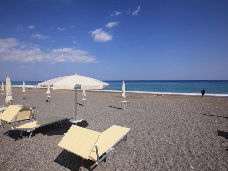 Leerer Strand mit hellen Liegestühlen, weißen Sonnenschirmen und blauem Himmel am Meer.