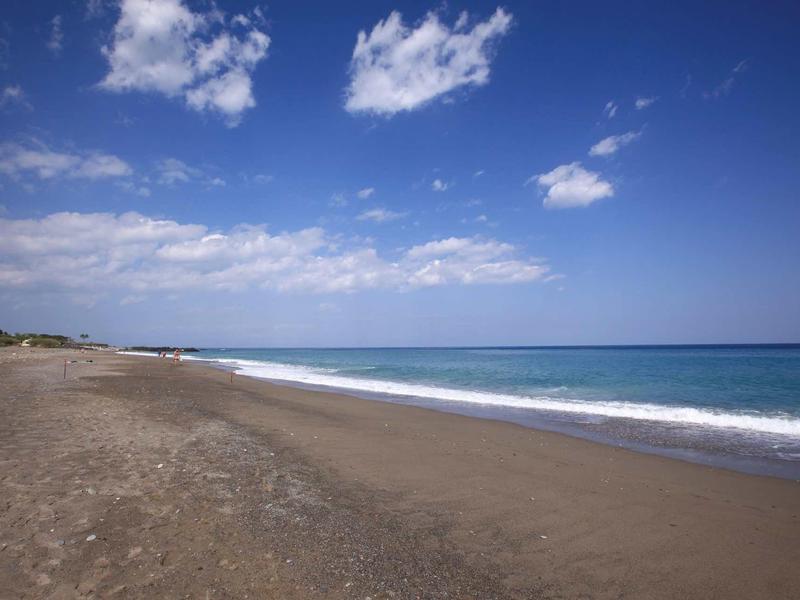Weite Sandstrand mit feinem Sand, blauem Meer und leicht bewölktem Himmel am Tag.