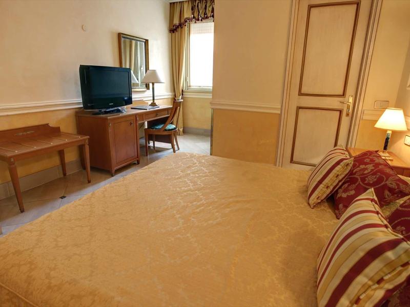 Gemütliches Schlafzimmer mit Doppelbett, Fernseher, Schreibtisch, Stuhl und Fenster mit Vorhang.