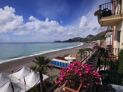 Balcony with blooming flowers overlooking beach and sea under a partly cloudy sky.