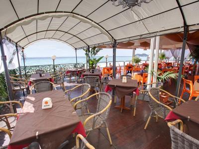 Covered restaurant terrace overlooking the sea with set tables.