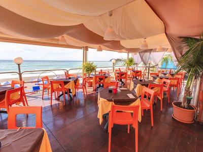 Open-air restaurant with orange chairs and sea view, covered by fabric roof.
