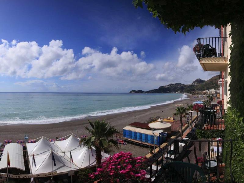 View of a calm beach with sun loungers and clear water under a blue sky.
