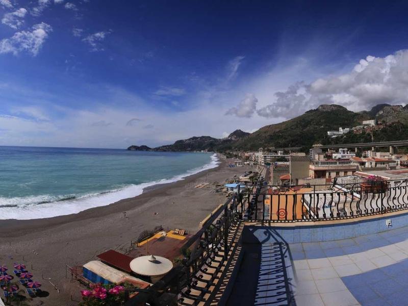 Panorama of a beach with umbrellas and mountains in the background under a blue sky.