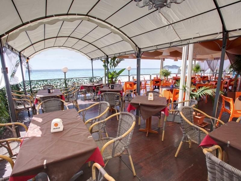 Covered restaurant terrace overlooking the sea with set tables.