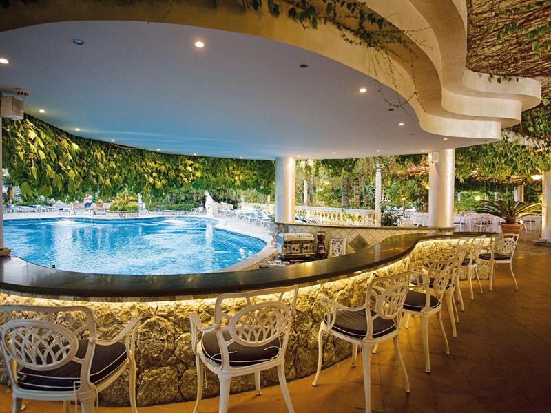 Bar avec tabourets et piscine illuminée dans un cadre hôtelier tropical la nuit.