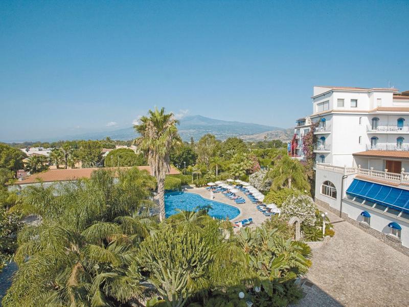 Hôtel avec piscine extérieure, palmiers et vue sur les collines sous un ciel bleu clair.