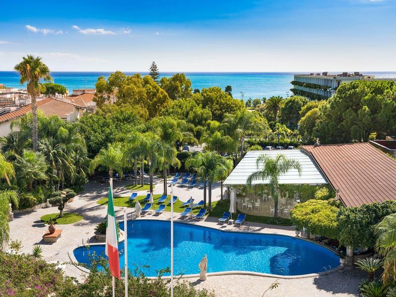Piscine avec parasols et palmiers, vue sur la mer et le ciel bleu.