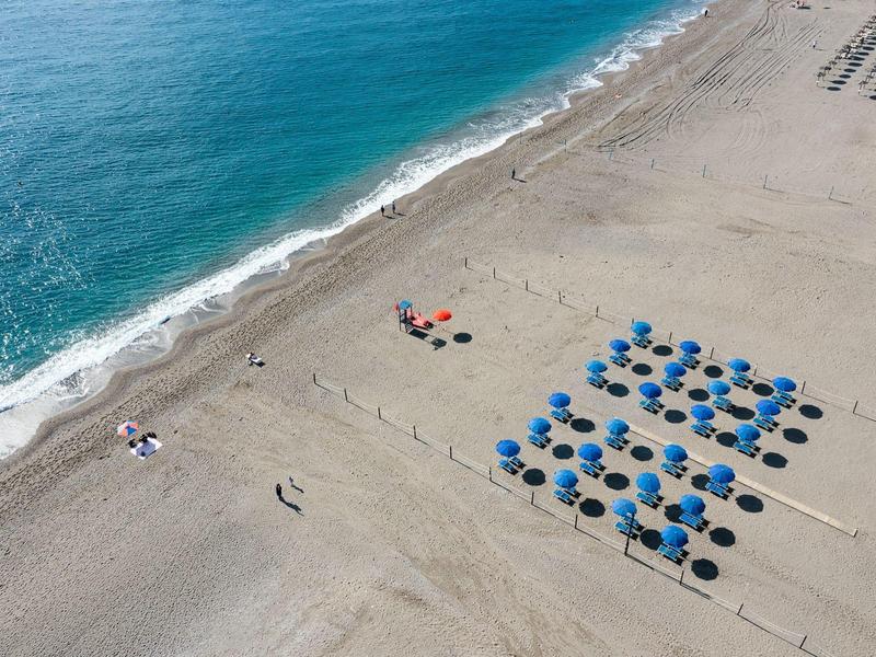 Plage de sable avec des parasols bleus et quelques personnes près du rivage.