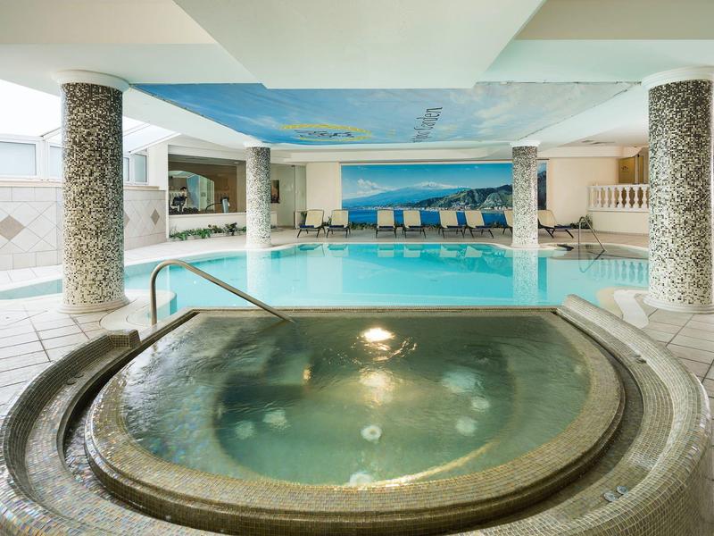 Piscine intérieure avec jacuzzi et chaises longues dans un espace bien-être lumineux.