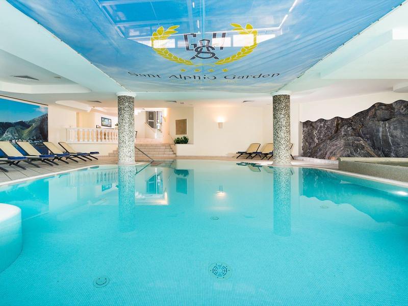 Piscine intérieure avec éclairage bleu, murs blancs, chaises longues et fresques murales.