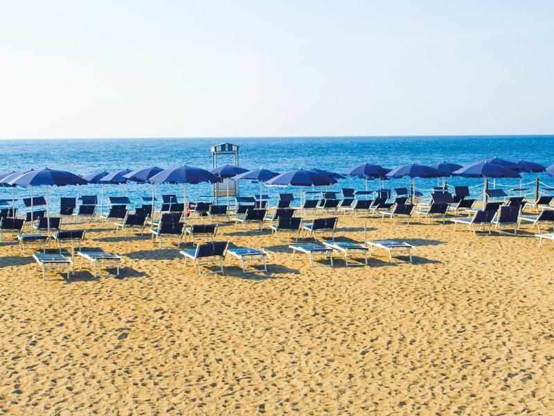 Plage de sable vide avec des rangées de parasols bleus et de chaises longues au bord de la mer.