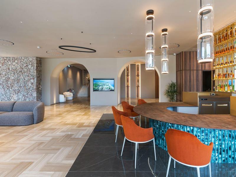 Salon d'hôtel moderne avec bar bleu, chaises orange et espaces de détente confortables.