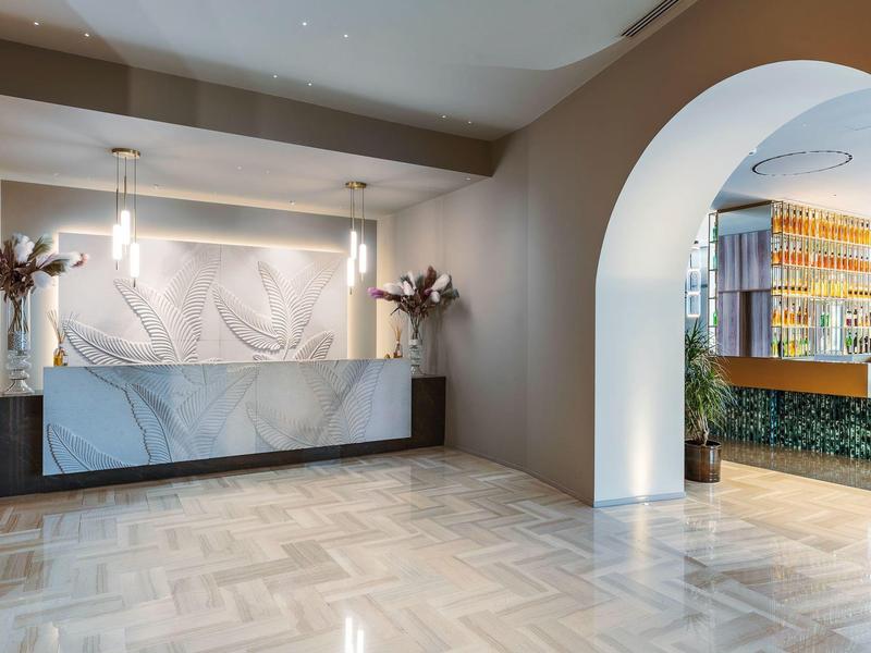 Hall d'hôtel moderne avec comptoir en marbre, murs clairs et plantes décoratives.