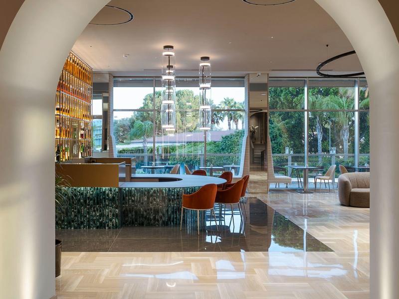 Espace bar d'hôtel moderne avec des chaises orange et vue sur une piscine extérieure à travers de grandes fenêtres.