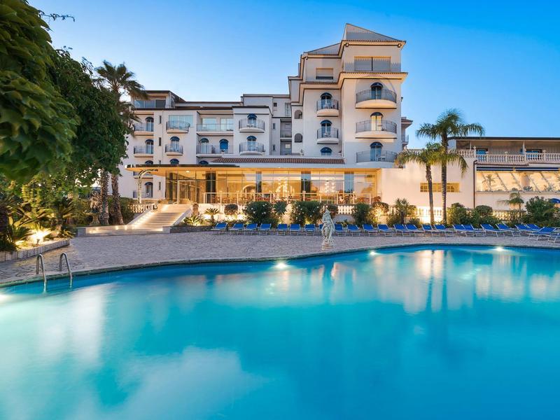 Hôtel de luxe avec piscine extérieure éclairée et palmiers au crépuscule.