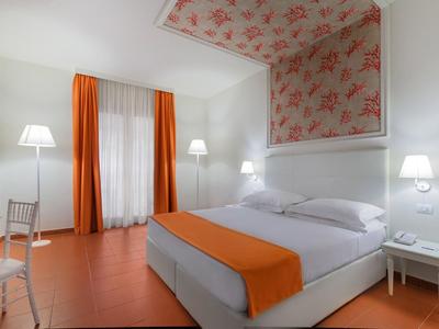 Bright hotel room with large bed, orange curtains, and floral wallpaper on the ceiling.