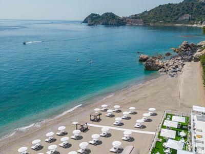 Beach with white umbrellas and clear blue water by a wooded coastline.