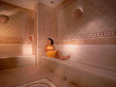 Woman relaxes in a warm-lit Turkish steam room with marble interior.